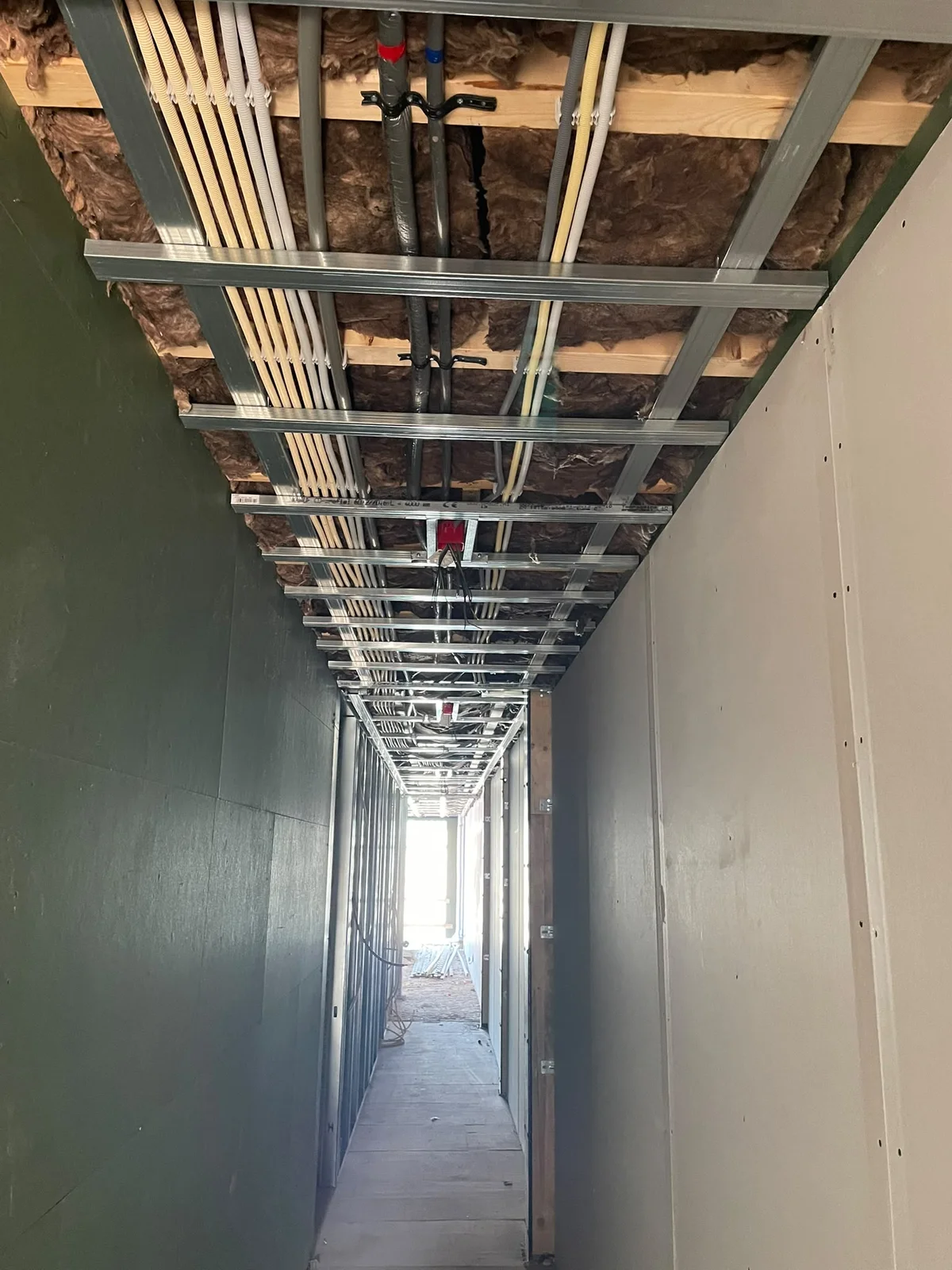 Leidingwerk boven een gang met metalstud plafond tijdens renovatie